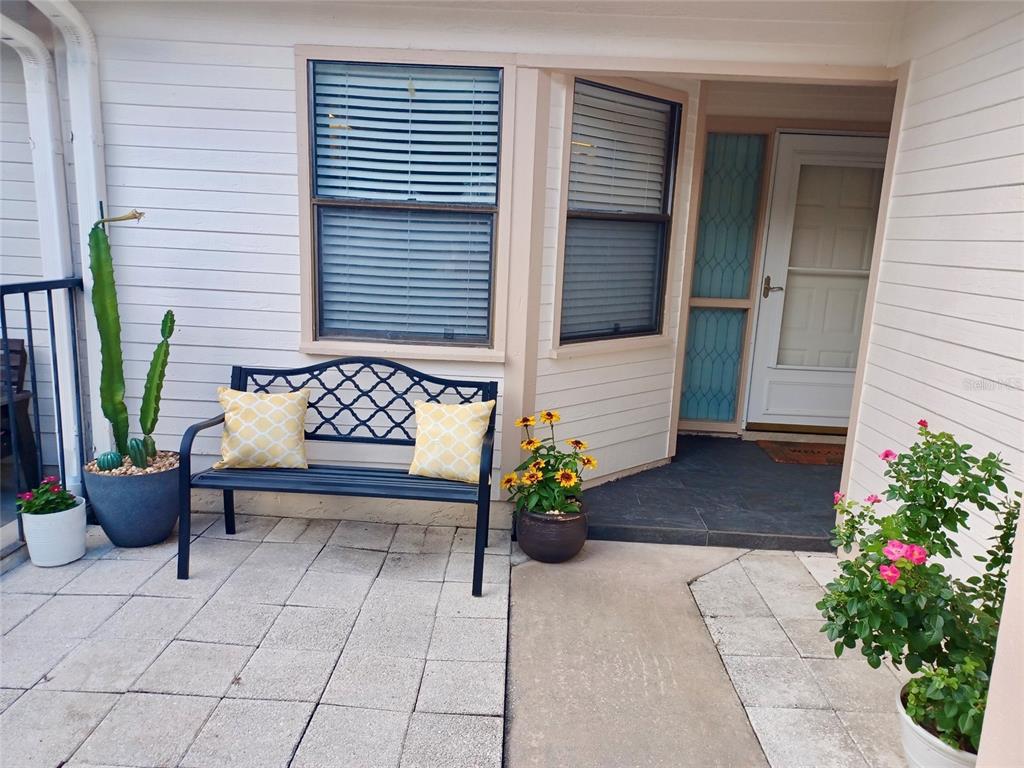 A patio features a black metal bench with yellow pillows, potted plants, and a front door — 3929 NE 21ST LANE, OCALA, FL