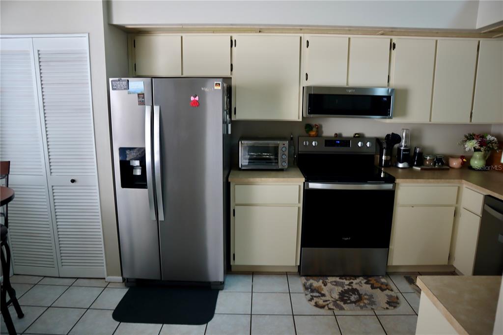 A kitchen features light-colored cabinets, stainless steel appliances, and white tiled flooring — 3929 NE 21ST LANE, OCALA, FL