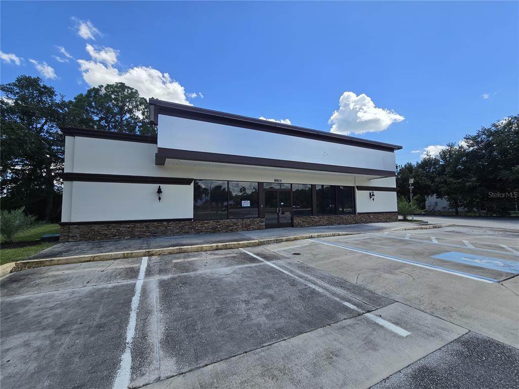 A single-story commercial building with a stone facade, glass storefront, and an adjacent parking lot — 8801 20TH STREET, VERO BEACH, FL