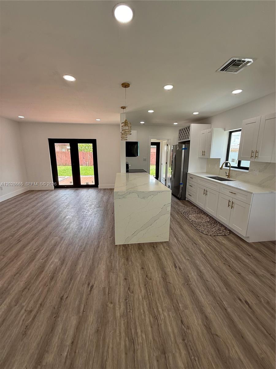 This open-concept kitchen features a large marble-topped island, white cabinetry, and wood-look flooring — 1014 W 66th St, Hialeah FL 33012, HIALEAH, FL