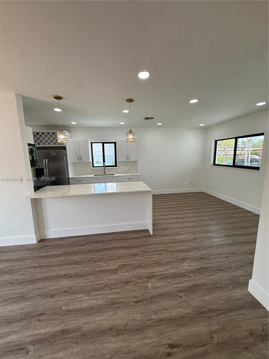 A modern kitchen features white cabinets, a quartz island, and wood-look flooring — 1014 W 66th St, Hialeah FL 33012, HIALEAH, FL