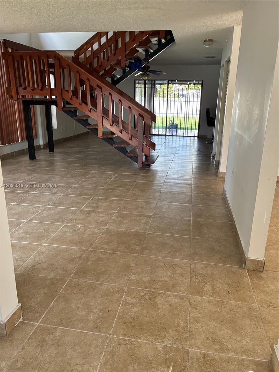 An open living area features tan tile floors and a wooden staircase with metal supports — 2441 SW 111th Ave # 2441, Miami FL 33165, MIAMI, FL