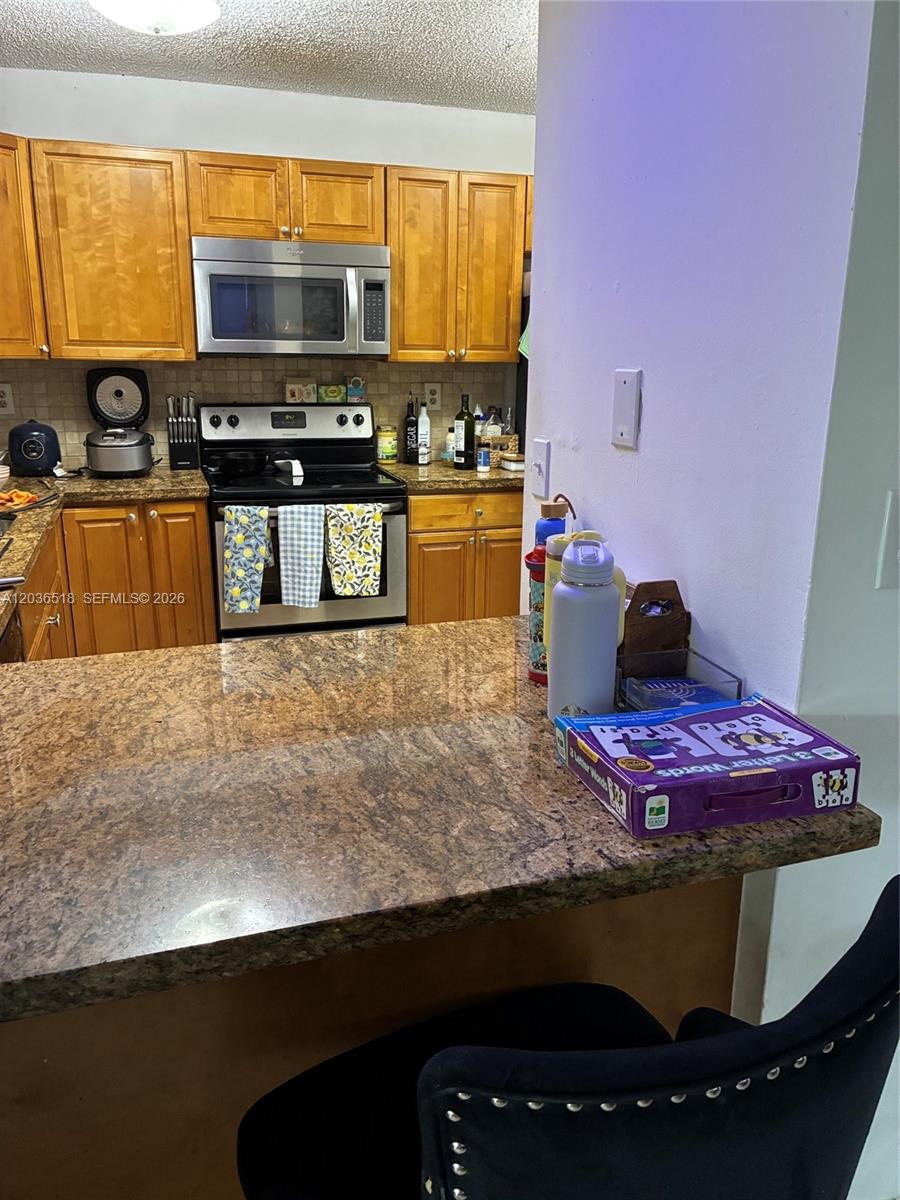 A kitchen features wood cabinets, granite countertops, a stainless steel microwave, and a black stove — 2441 SW 111th Ave # 2441, Miami FL 33165, MIAMI, FL