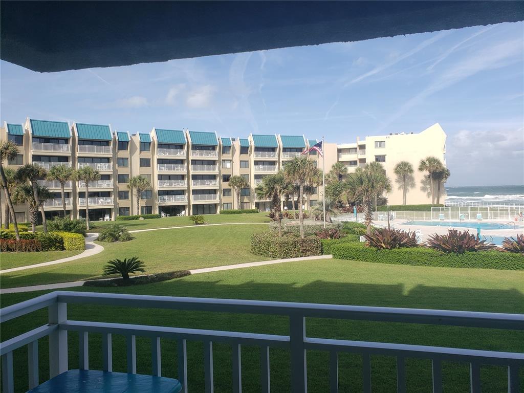 A balcony view overlooking a grassy courtyard, swimming pool, and the ocean beyond — 4501 S ATLANTIC AVENUE UNIT 205, NEW SMYRNA BEACH, FL