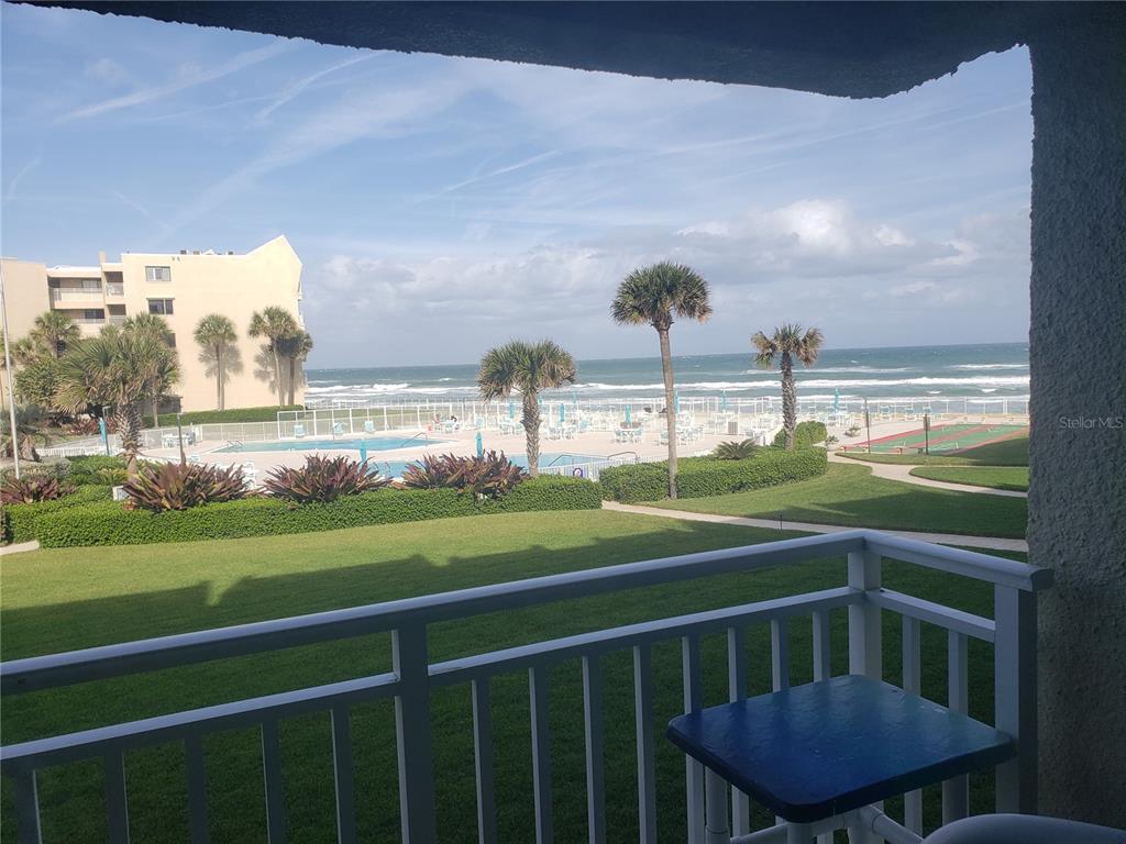 A balcony overlooks a grassy lawn, a swimming pool, palm trees, and the ocean — 4501 S ATLANTIC AVENUE UNIT 205, NEW SMYRNA BEACH, FL
