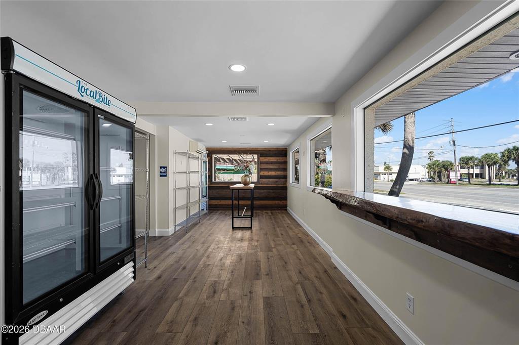 A commercial space features wood-look flooring, a glass-door refrigerator, and a window-side counter — 819 SR A1A HIGHWAY, NEW SMYRNA BEACH, FL