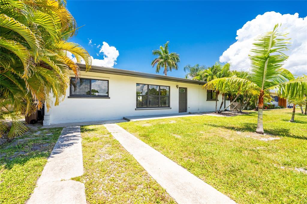 A single-story white house with a flat roof, concrete driveway, and surrounding palm trees — 410 W GRACE STREET, PUNTA GORDA, FL