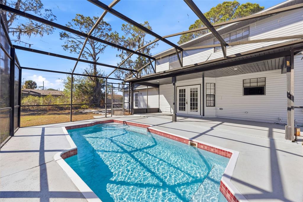 A swimming pool with red tile trim sits on a patio enclosed by a screen — 33710 LINDA LANE, LEESBURG, FL