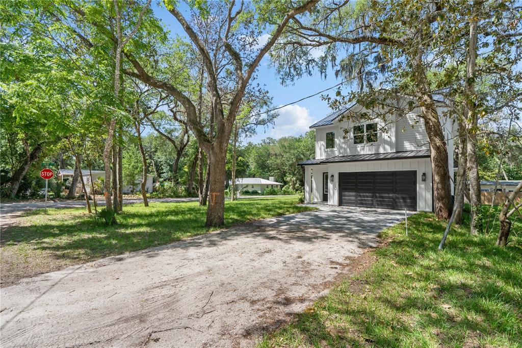 A two-story white house with a dark metal roof and garage sits on a dirt driveway — 2 SANCHEZ AVENUE, PALM COAST, FL