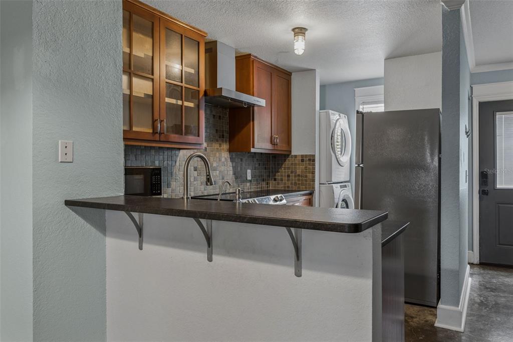 A kitchen features wood cabinets, a tiled backsplash, a dark countertop, and a stacked washer-dryer — 5720 DALDEN DRIVE UNIT 5720, TAMPA, FL