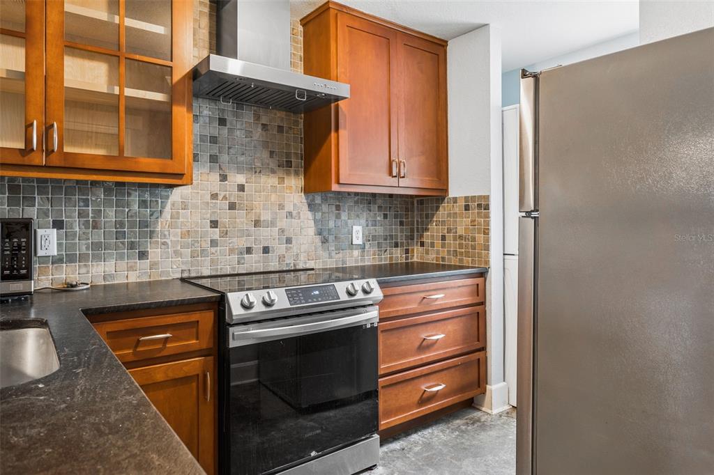 A kitchen features wood cabinets, a stainless steel range, and a mosaic tile backsplash — 5720 DALDEN DRIVE UNIT 5720, TAMPA, FL