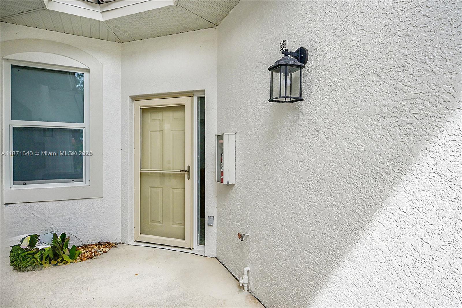 A beige storm door is set into a white stucco wall with a wall-mounted lantern — 4700 YACHT HARBOR DR # 612, Naples FL 34112, NAPLES, FL