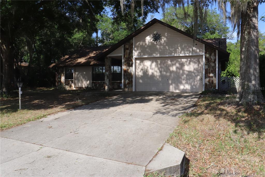 A single-story house with a stone facade, beige siding, and a two-car garage — 1112 NE 130 TERRACE, SILVER SPRINGS, FL