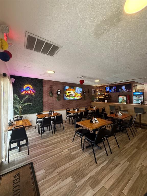 A restaurant dining area features wood-look tile flooring, brick walls, and several tables with chairs — 36657 US HIGHWAY 19 N, PALM HARBOR, FL