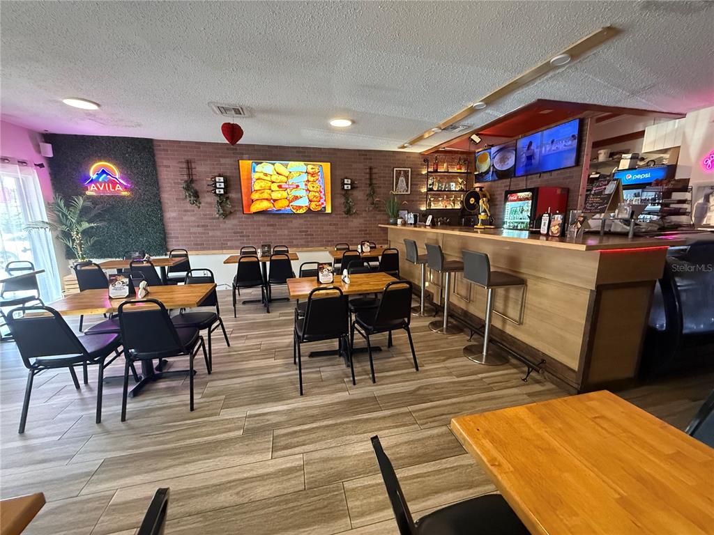 A restaurant interior features a wooden bar, tables with black chairs, and brick accent walls — 36657 US HIGHWAY 19 N, PALM HARBOR, FL