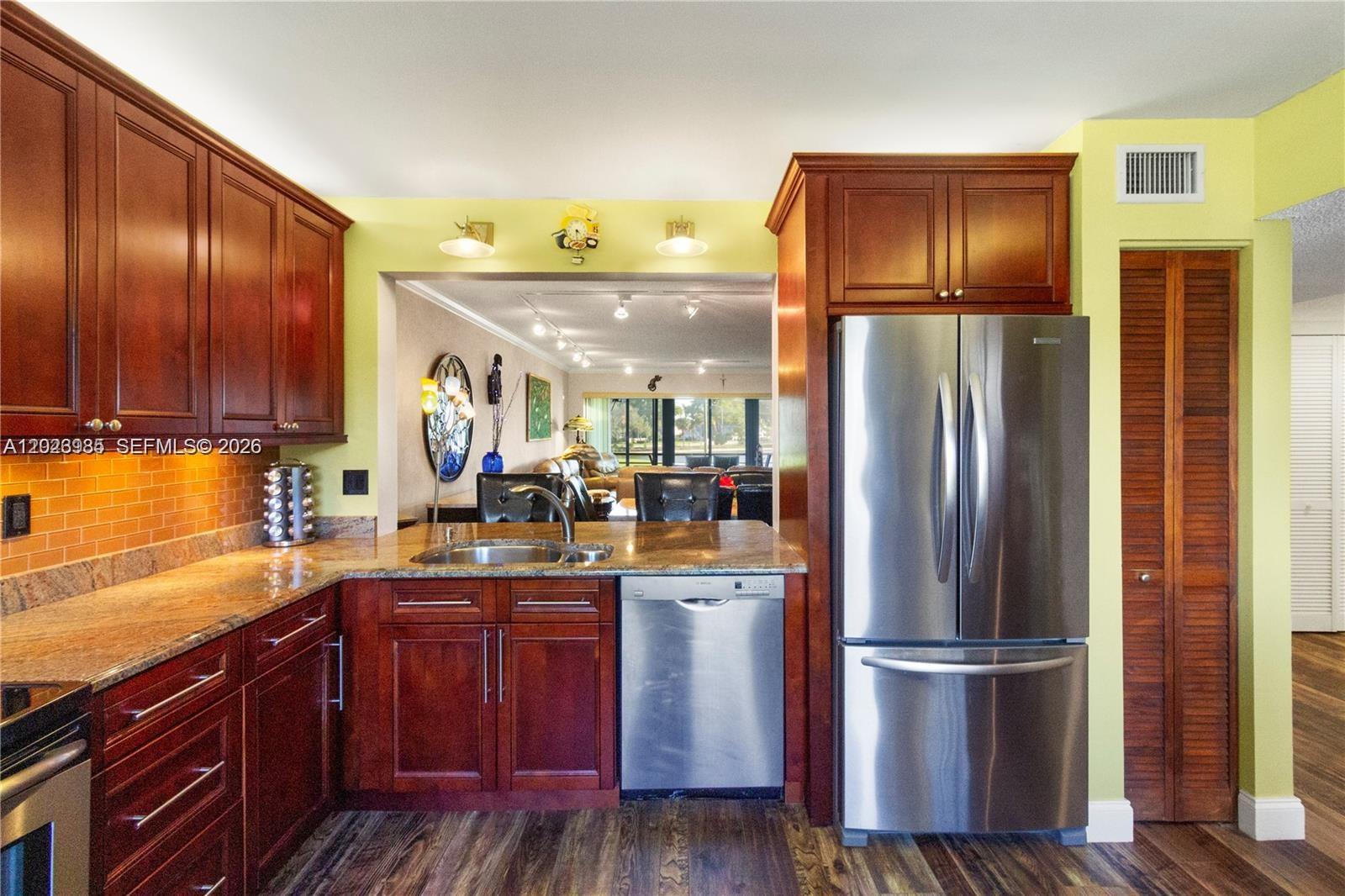 A kitchen features dark wood cabinets, granite countertops, stainless steel appliances, and yellow walls — 5519 FAIRWAY PARK DR # 203, Boynton Beach FL 33437, BOYNTON BEACH, FL