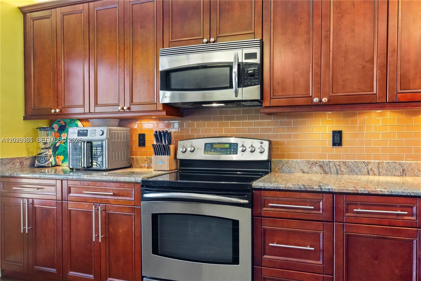 A kitchen features cherry wood cabinets, stainless steel appliances, and a tan subway tile backsplash — 5519 FAIRWAY PARK DR # 203, Boynton Beach FL 33437, BOYNTON BEACH, FL