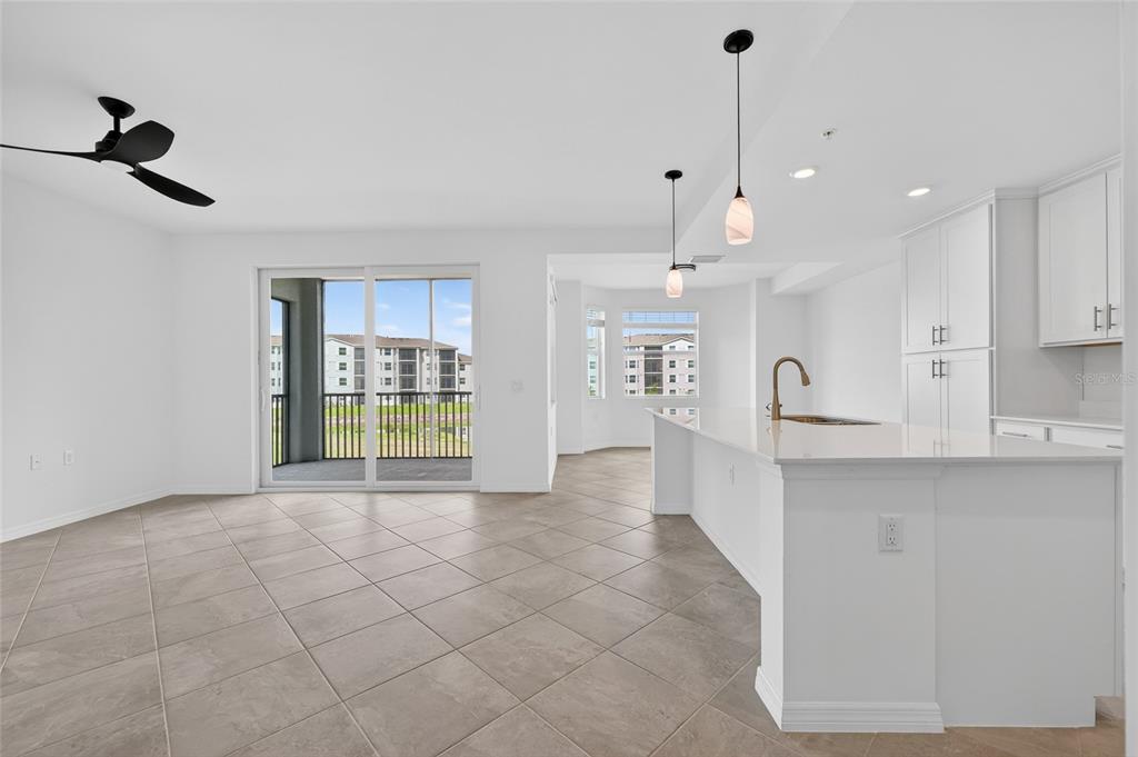 A bright, open-concept kitchen and living area with white cabinetry, tile flooring, and sliding doors — 18461 COPPERHEAD COURT N UNIT 422, LEHIGH ACRES, FL