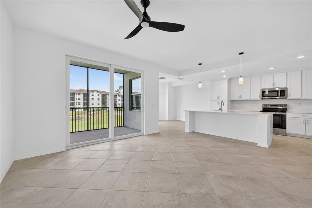 An open-concept kitchen and living area with tile floors, white cabinetry, and a sliding glass door — 18461 COPPERHEAD COURT N UNIT 422, LEHIGH ACRES, FL