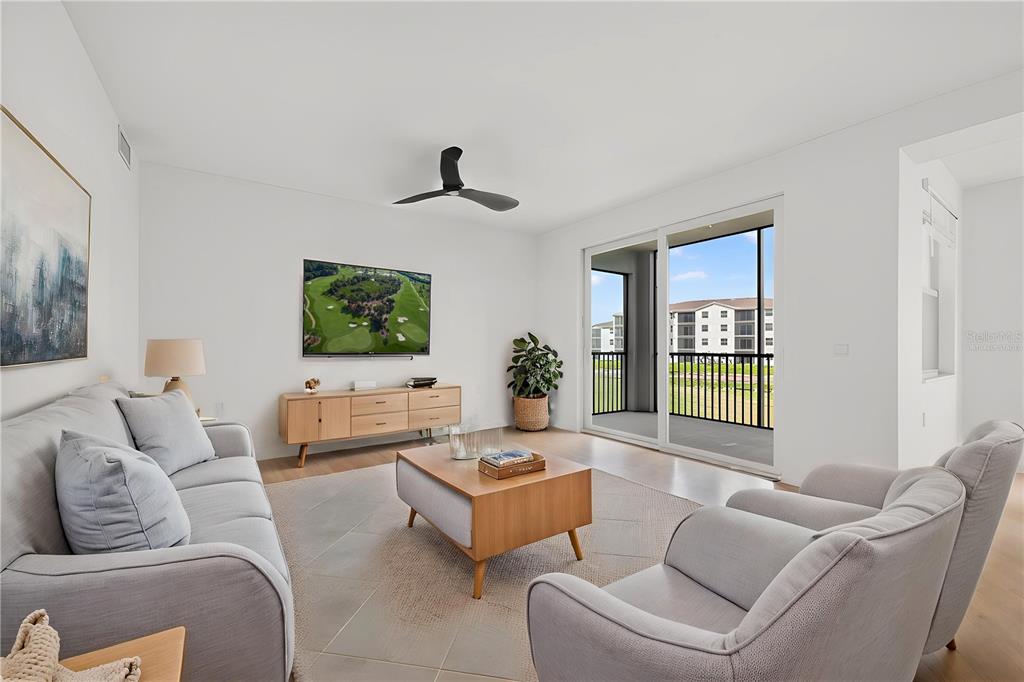 A living room features light gray furniture, a wooden media console, and a balcony view — 18461 COPPERHEAD COURT N UNIT 422, LEHIGH ACRES, FL