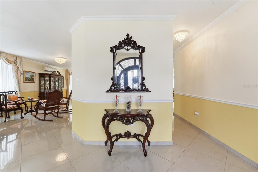 A foyer features a dark wood console table and ornate mirror against a yellow wall — 644 HELICONIA, SAN JUAN, PR