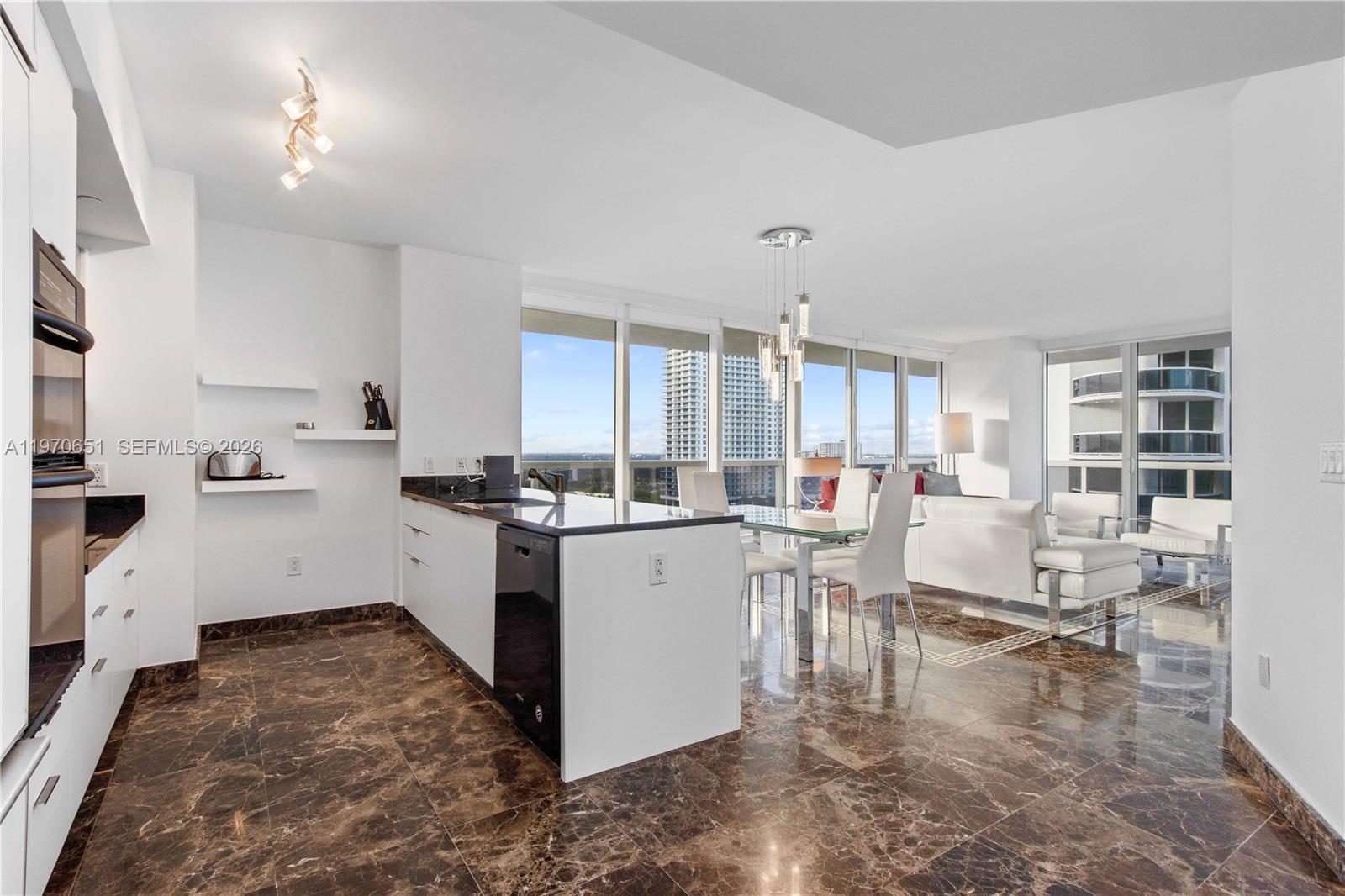 A modern kitchen and dining area feature dark marble floors, white cabinetry, and floor-to-ceiling windows — 1830 S Ocean Dr # 1908, Hallandale Beach FL 33009, HALLANDALE BEACH, FL