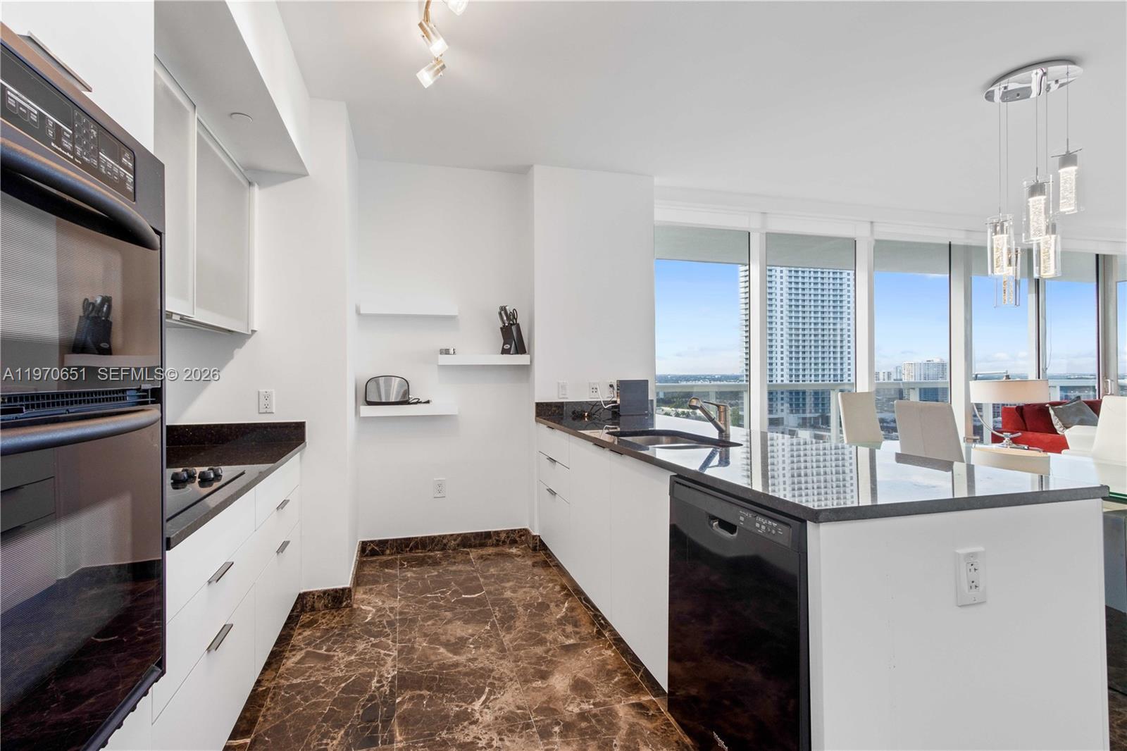A modern kitchen features white cabinetry, dark granite countertops, and brown marble flooring — 1830 S Ocean Dr # 1908, Hallandale Beach FL 33009, HALLANDALE BEACH, FL