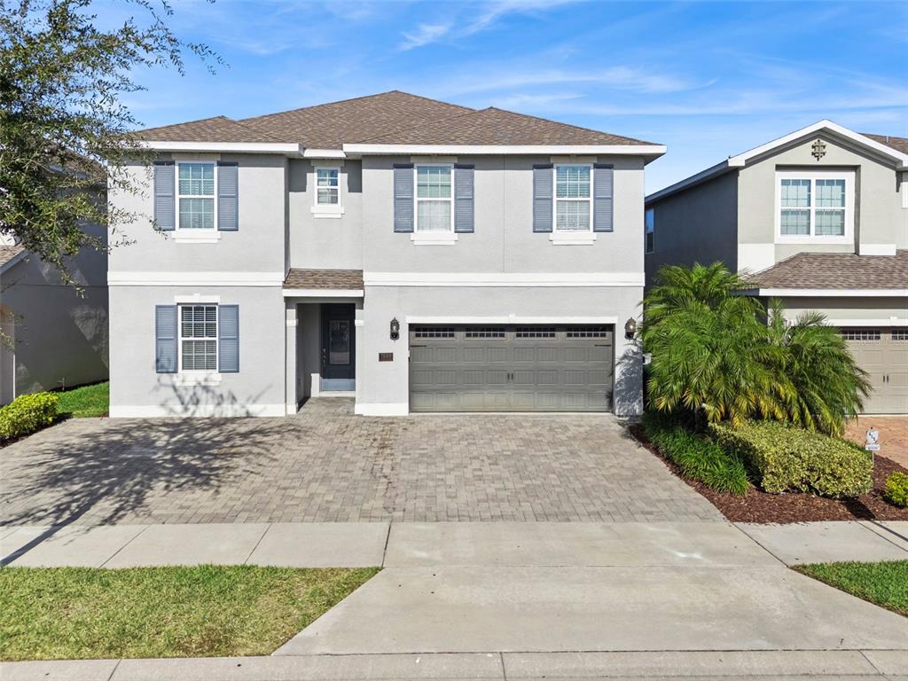 A two-story gray house with a paver driveway, a two-car garage, and blue shutters — 7649 FAIRFAX DRIVE, KISSIMMEE, FL