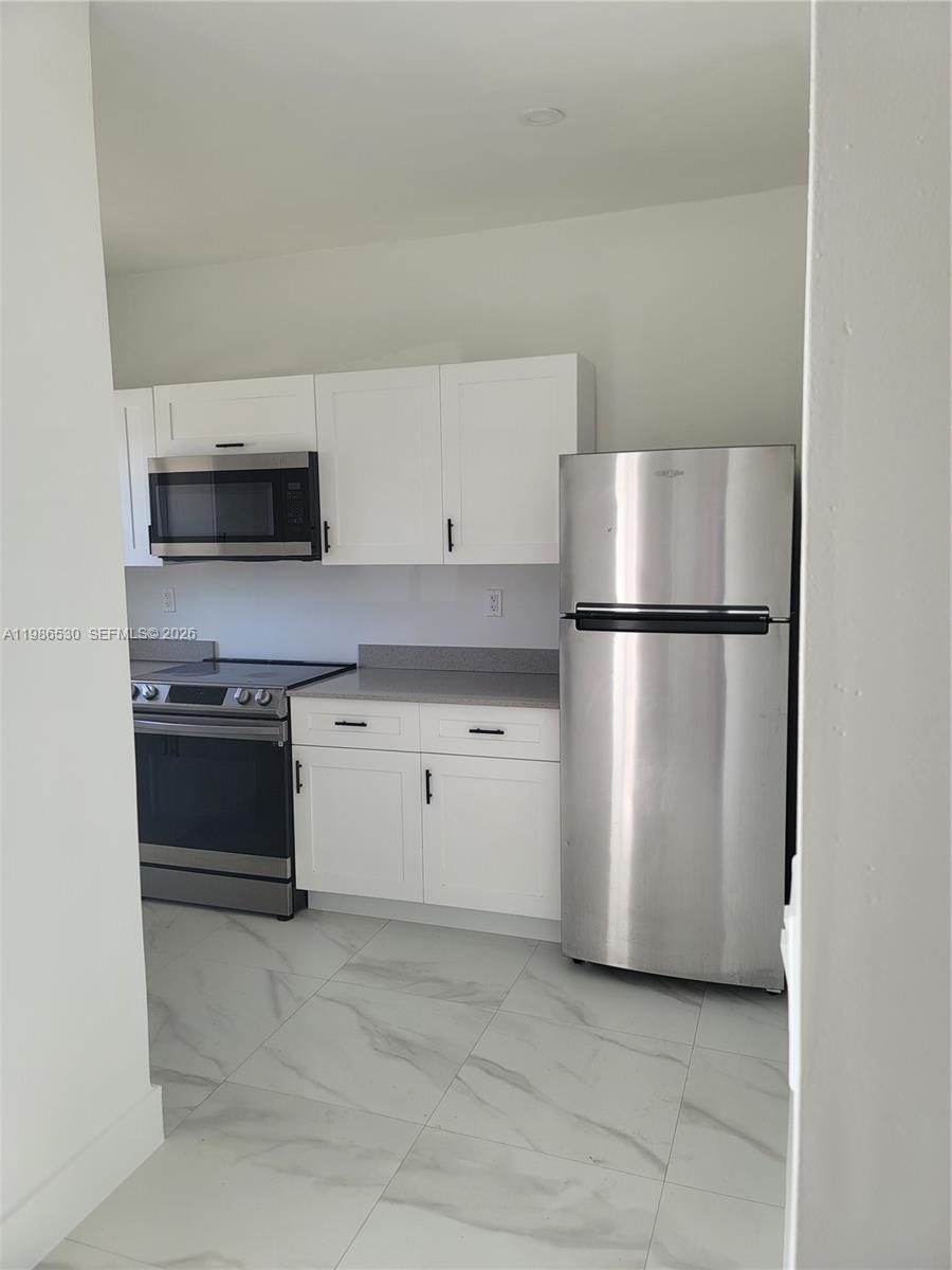 A kitchen features white cabinets, stainless steel appliances, gray countertops, and light marble-patterned tile flooring — 1975 NW 24th Ct, Miami FL 33125, MIAMI, FL