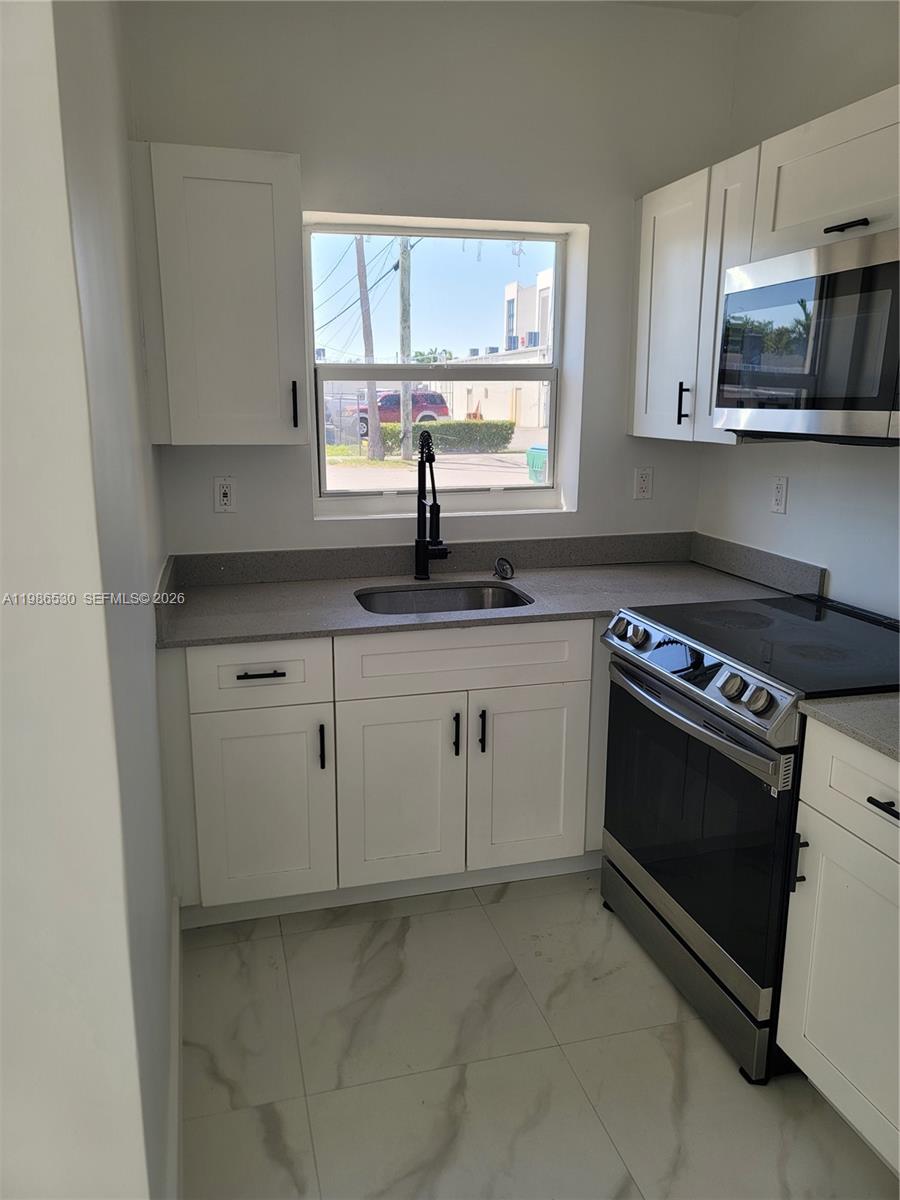 A small kitchen features white cabinets, a stainless steel microwave, and a gray countertop — 1975 NW 24th Ct, Miami FL 33125, MIAMI, FL