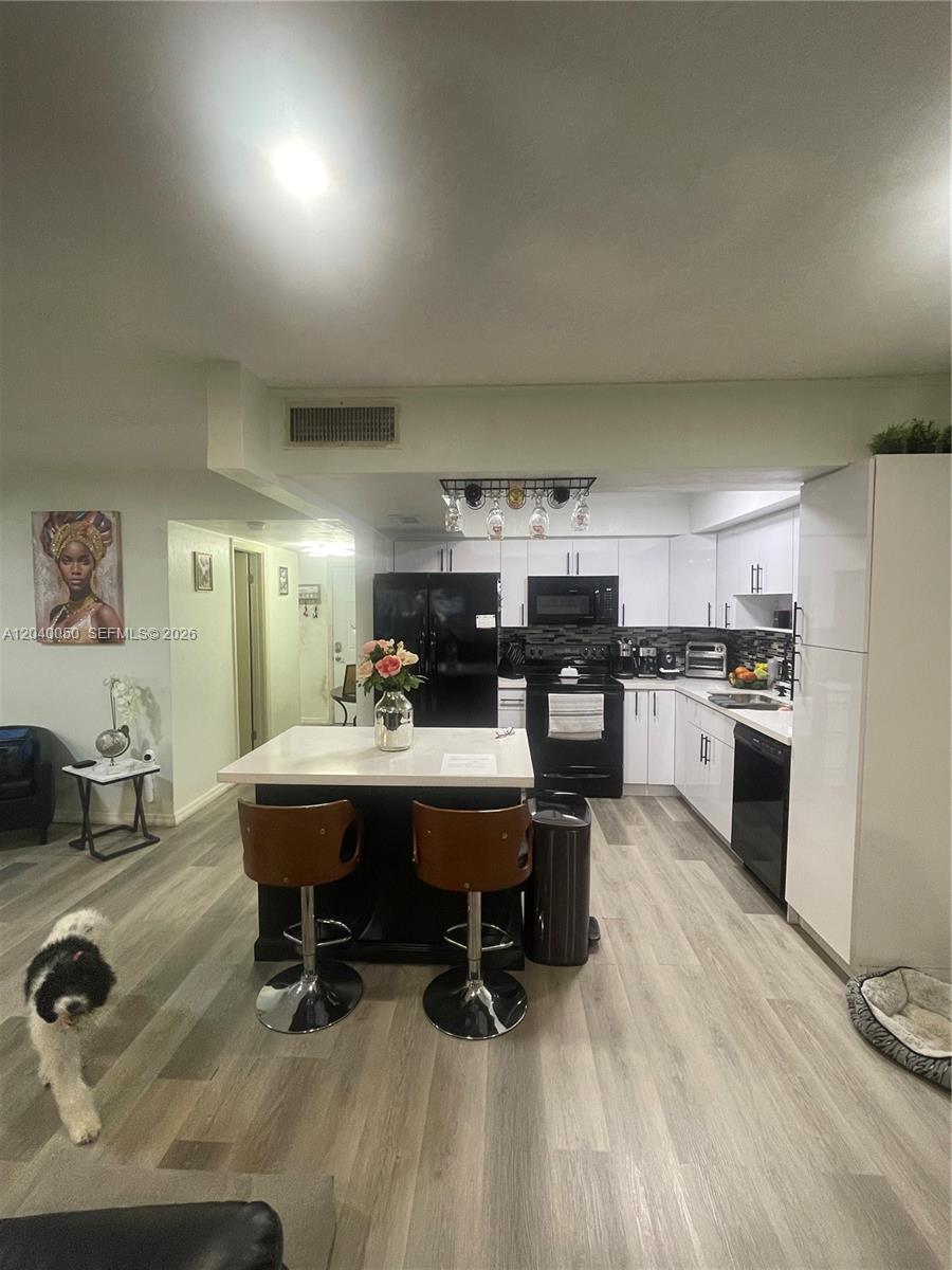 A kitchen with white cabinets, black appliances, and a central island with two bar stools — 6945 W 2nd Way, Hialeah FL 33014, HIALEAH, FL