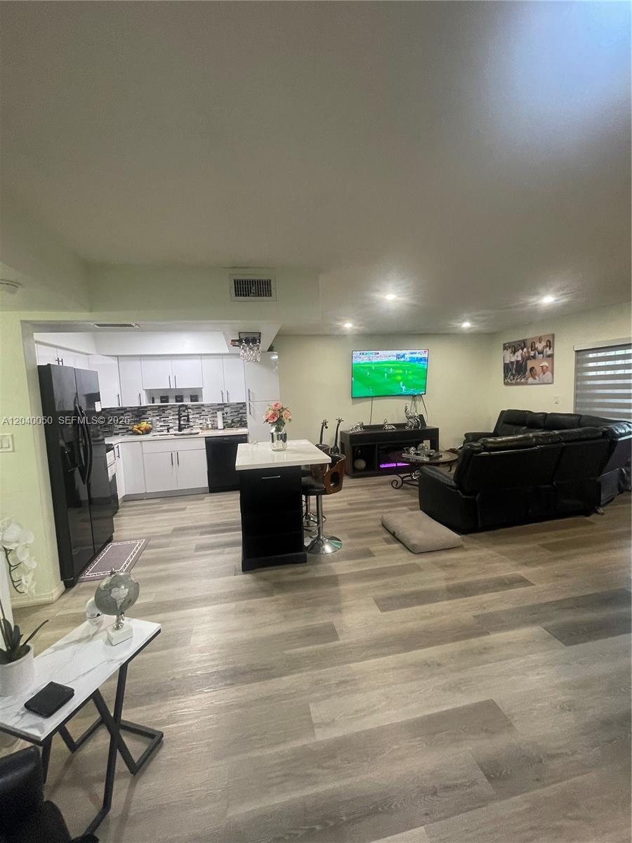 An open-concept living room and kitchen featuring white cabinets, a black island, and wood-look flooring — 6945 W 2nd Way, Hialeah FL 33014, HIALEAH, FL