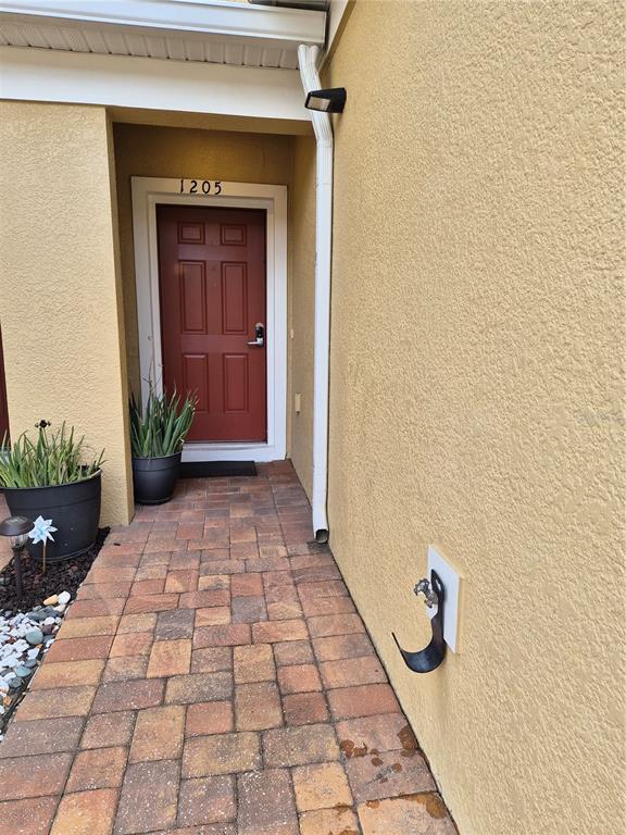 A red front door with a house number sits at the end of a brick walkway — 1205 TETON DRIVE, KISSIMMEE, FL