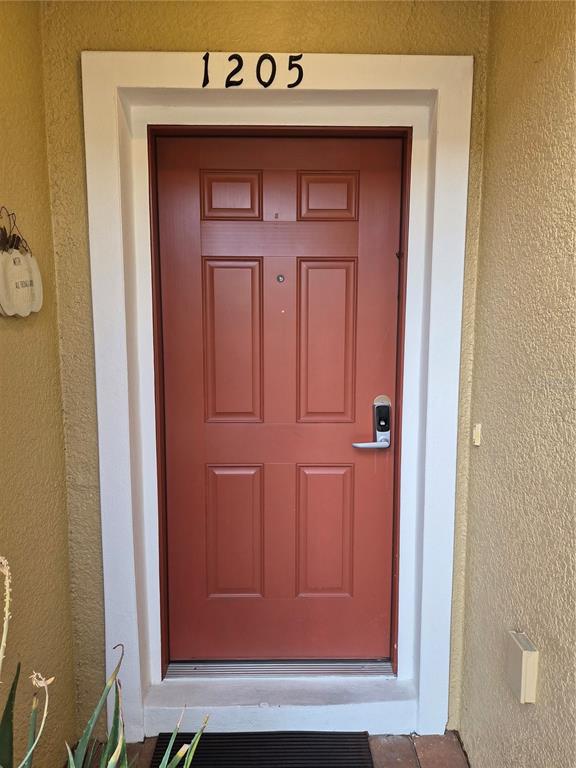 A red front door with a digital lock is set within a white frame — 1205 TETON DRIVE, KISSIMMEE, FL