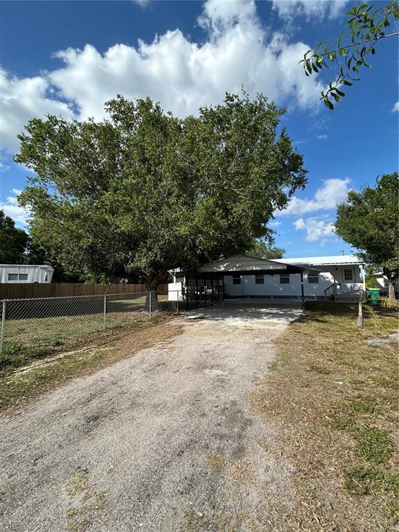 A white mobile home with a carport sits behind a gravel driveway and large tree — 5522 SWAYING PALM, PUNTA GORDA, FL