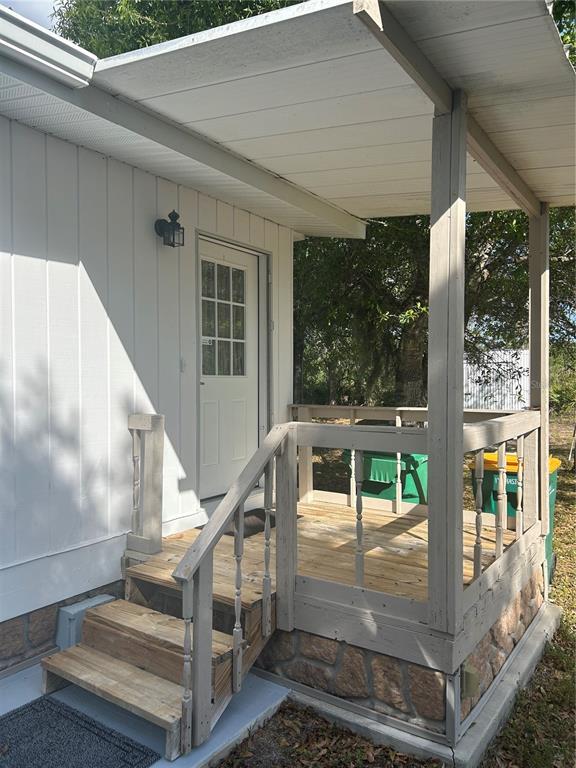 A white exterior wall with a small wooden porch, stairs, and a glass-paneled entry door — 5522 SWAYING PALM, PUNTA GORDA, FL