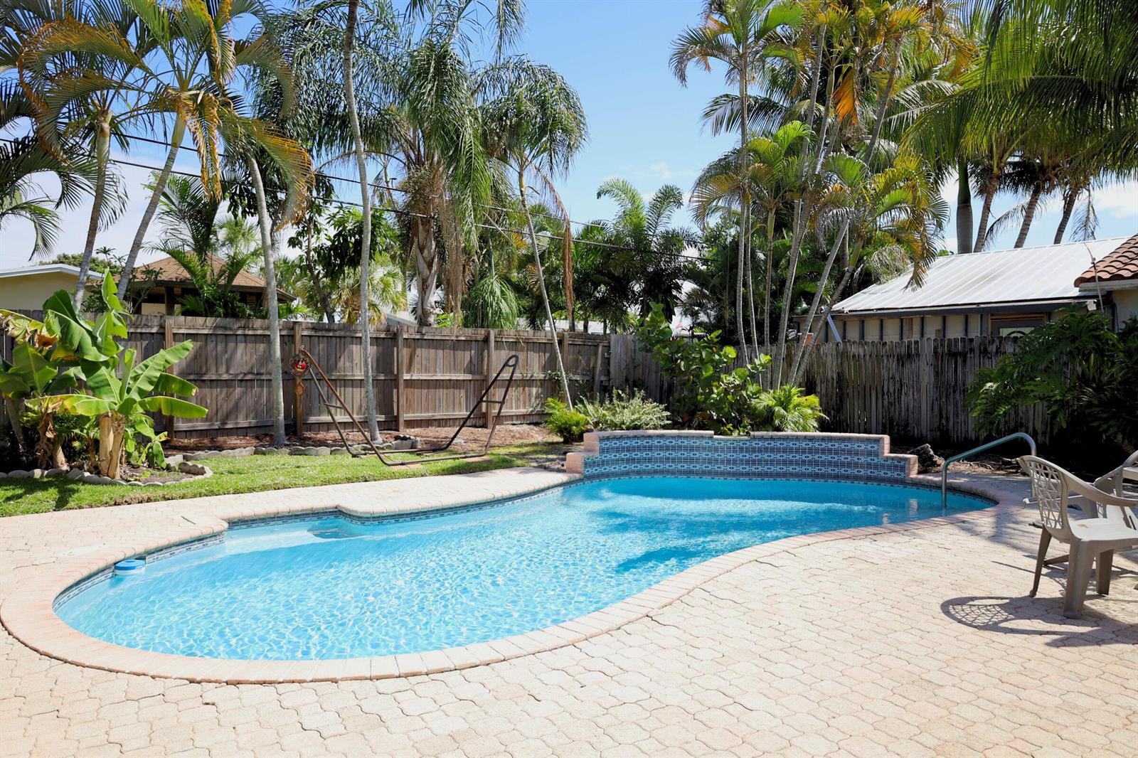 A backyard features a kidney-shaped swimming pool with a tiled wall, surrounded by paver decking — 1259 SW 7th Street, Boca Raton FL 33486, BOCA RATON, FL
