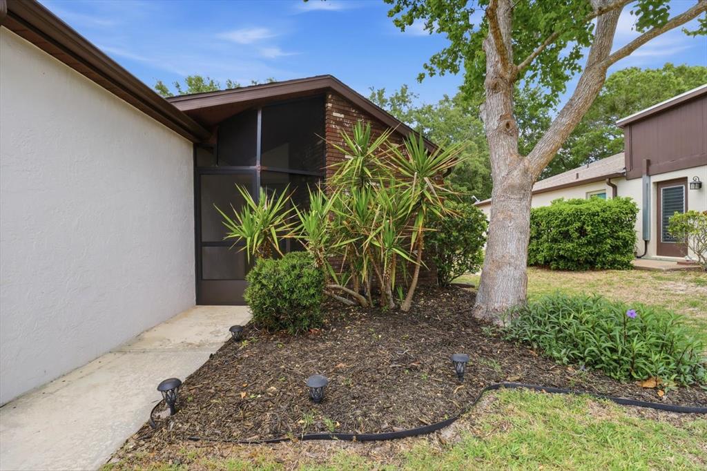 A view of a home exterior featuring a screened entryway, brick accents, and landscaped garden — 54 JAMAICA STREET, HOMOSASSA, FL