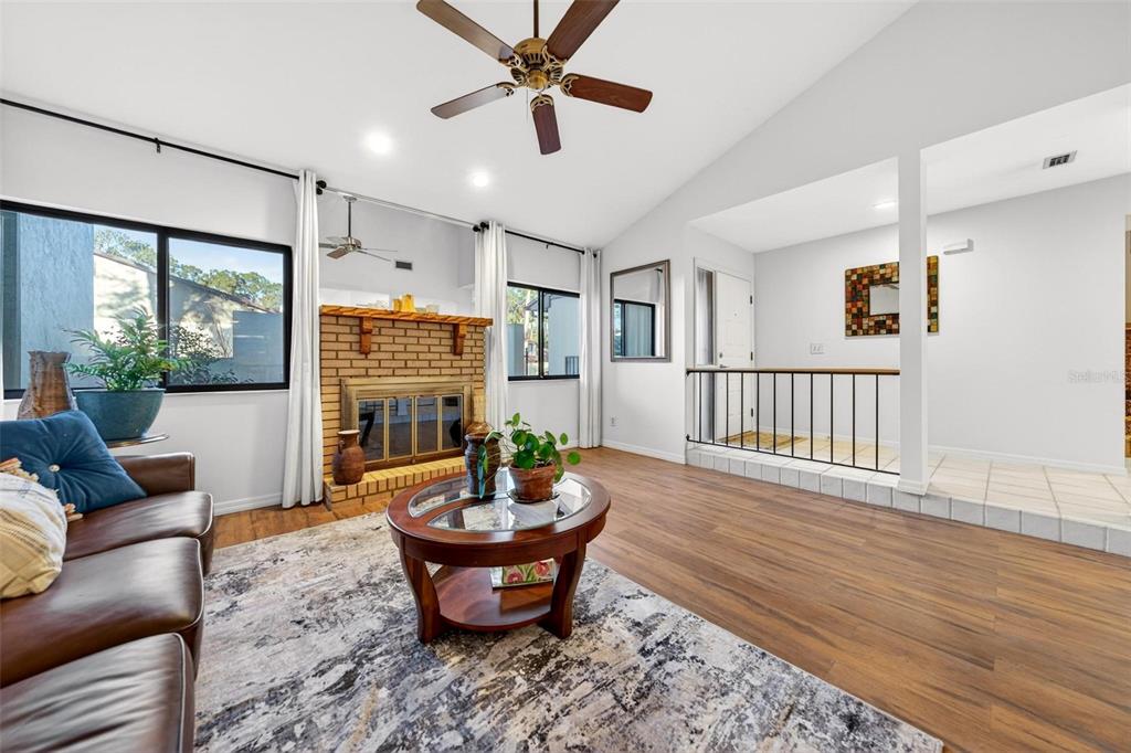A living room with a brick fireplace, wood-look flooring, and an elevated entryway with railings — 3804 NE 17TH STREET, OCALA, FL