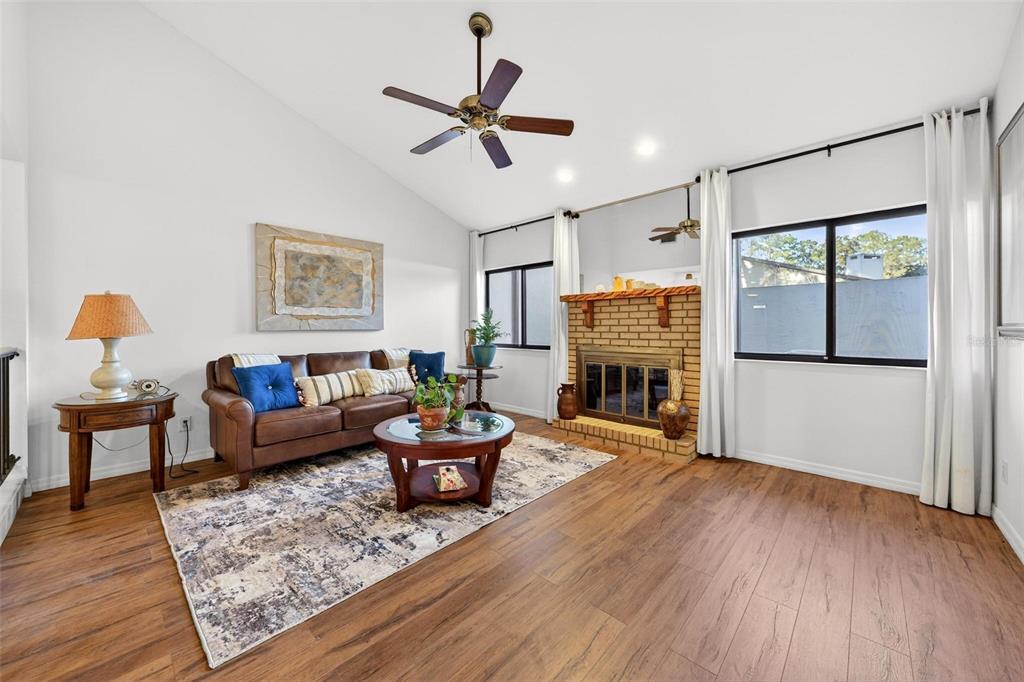 A living room features wood-look flooring, a brick fireplace, a brown sofa, and vaulted ceilings — 3804 NE 17TH STREET, OCALA, FL