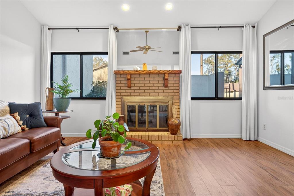 A living room features a brick fireplace, wood-look flooring, and large windows with white curtains — 3804 NE 17TH STREET, OCALA, FL