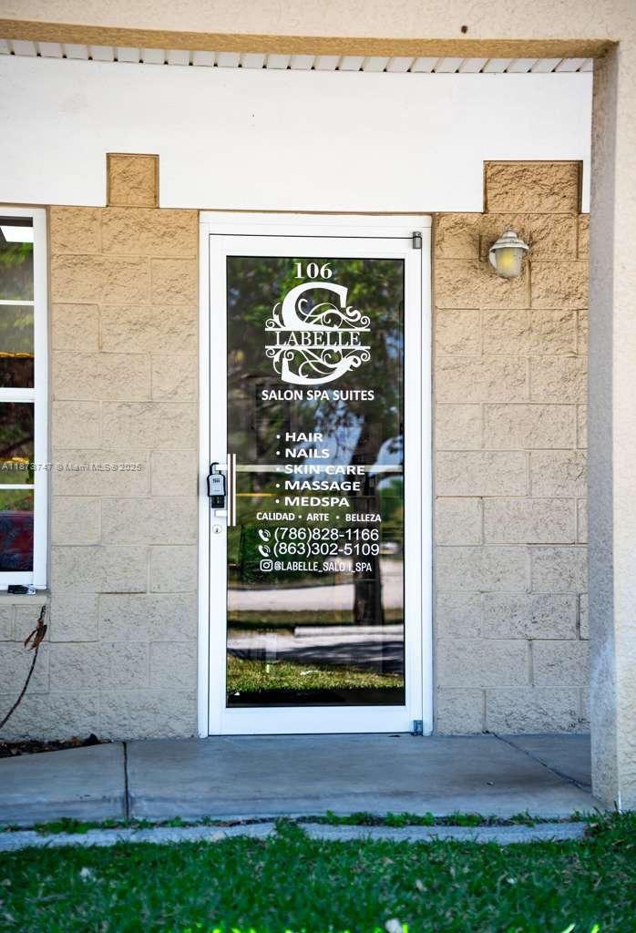 The exterior view shows a glass door to a salon spa suite numbered 106 — 825 E COWBOY WAY, La Belle FL 33935, LA BELLE, FL