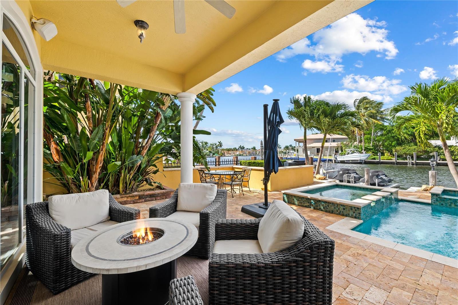 A covered patio features a fire pit, wicker seating, and a pool overlooking a canal — 2637 NE 28th Court, Lighthouse Point FL 33064, LIGHTHOUSE POINT, FL