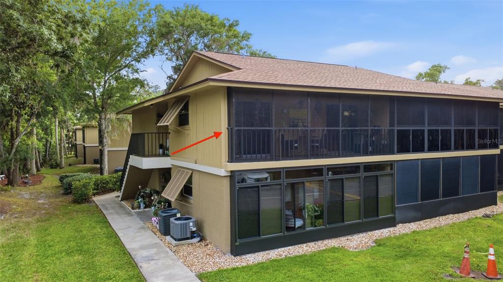 An exterior view of a two-story building featuring a screened-in balcony and ground-level patio — 140 ORCHID WOODS COURT UNIT 13B, DELTONA, FL