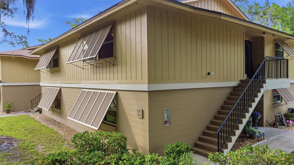 An exterior view of a two-story apartment building with tan siding and metal window awnings — 140 ORCHID WOODS COURT UNIT 13B, DELTONA, FL