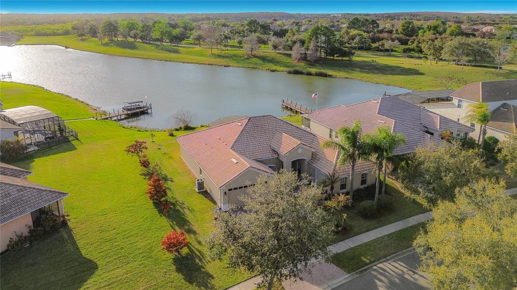 An aerial view shows a tan house with a tiled roof situated beside a lake — 3508 SUNSET ISLES BOULEVARD, KISSIMMEE, FL