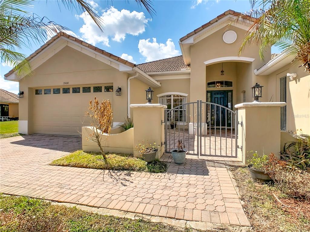 A tan house with a paved driveway, a gated courtyard, and a two-car garage — 3508 SUNSET ISLES BOULEVARD, KISSIMMEE, FL