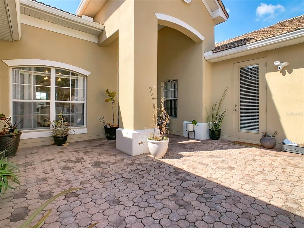 A paved courtyard features potted plants, a large arched window, and a glass-paneled door — 3508 SUNSET ISLES BOULEVARD, KISSIMMEE, FL