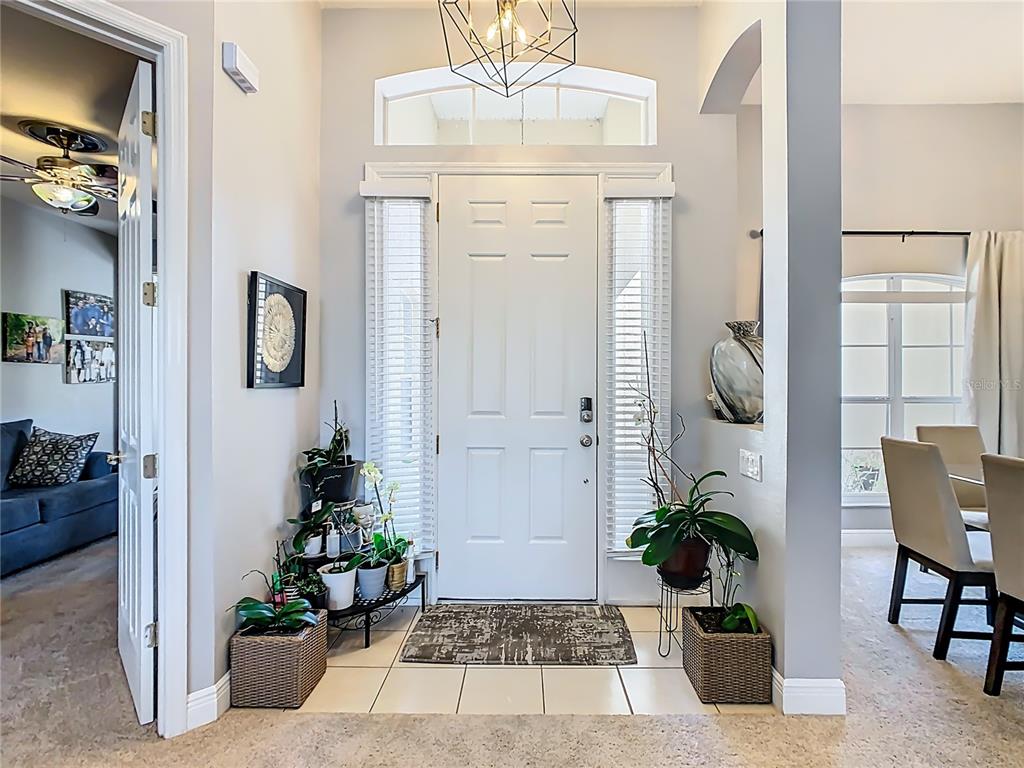 A bright entryway features a white front door with sidelights, tile flooring, and potted plants — 3508 SUNSET ISLES BOULEVARD, KISSIMMEE, FL