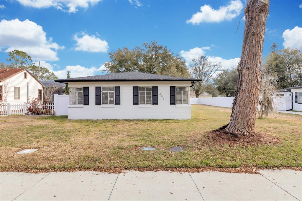 A white, single-story house with black shutters and a dark roof sits on a lawn — 307 E MONUMENT AVENUE UNIT A, KISSIMMEE, FL